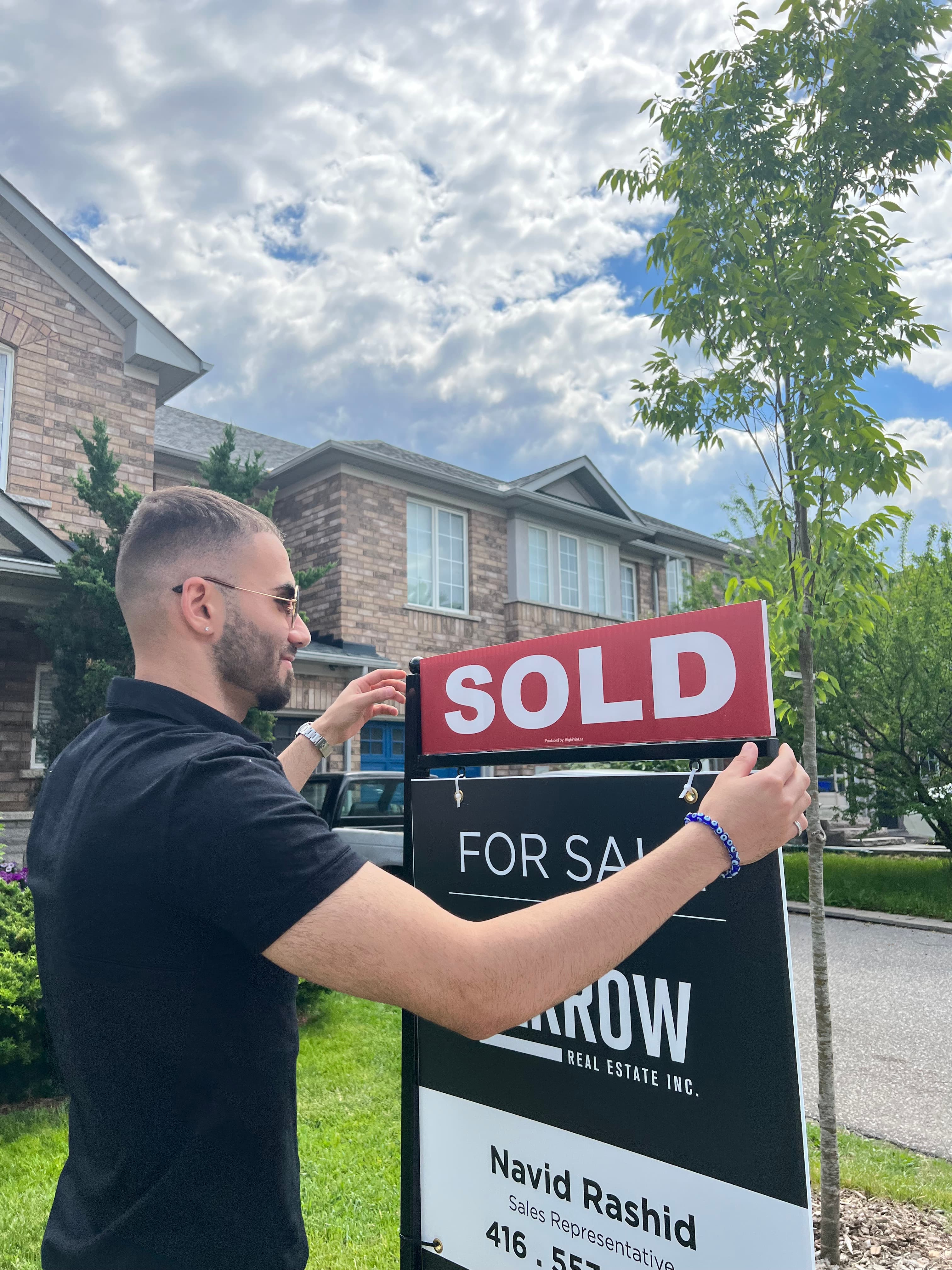 Navid Rashid placing a sold topper on a Ferrow Real Estate sign